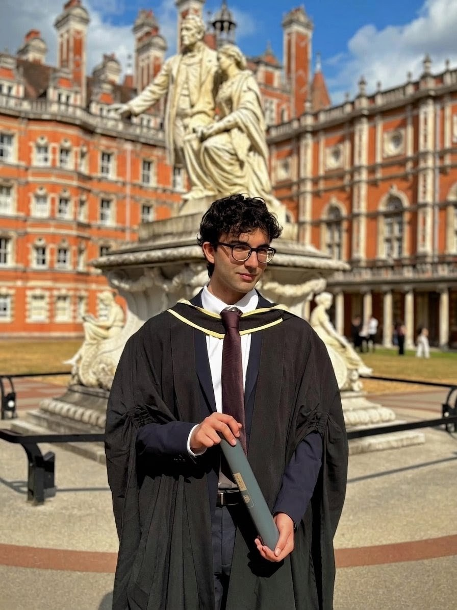 Sinan in cap and gown on graduation day, outside the Founder's Building at Royal Holloway